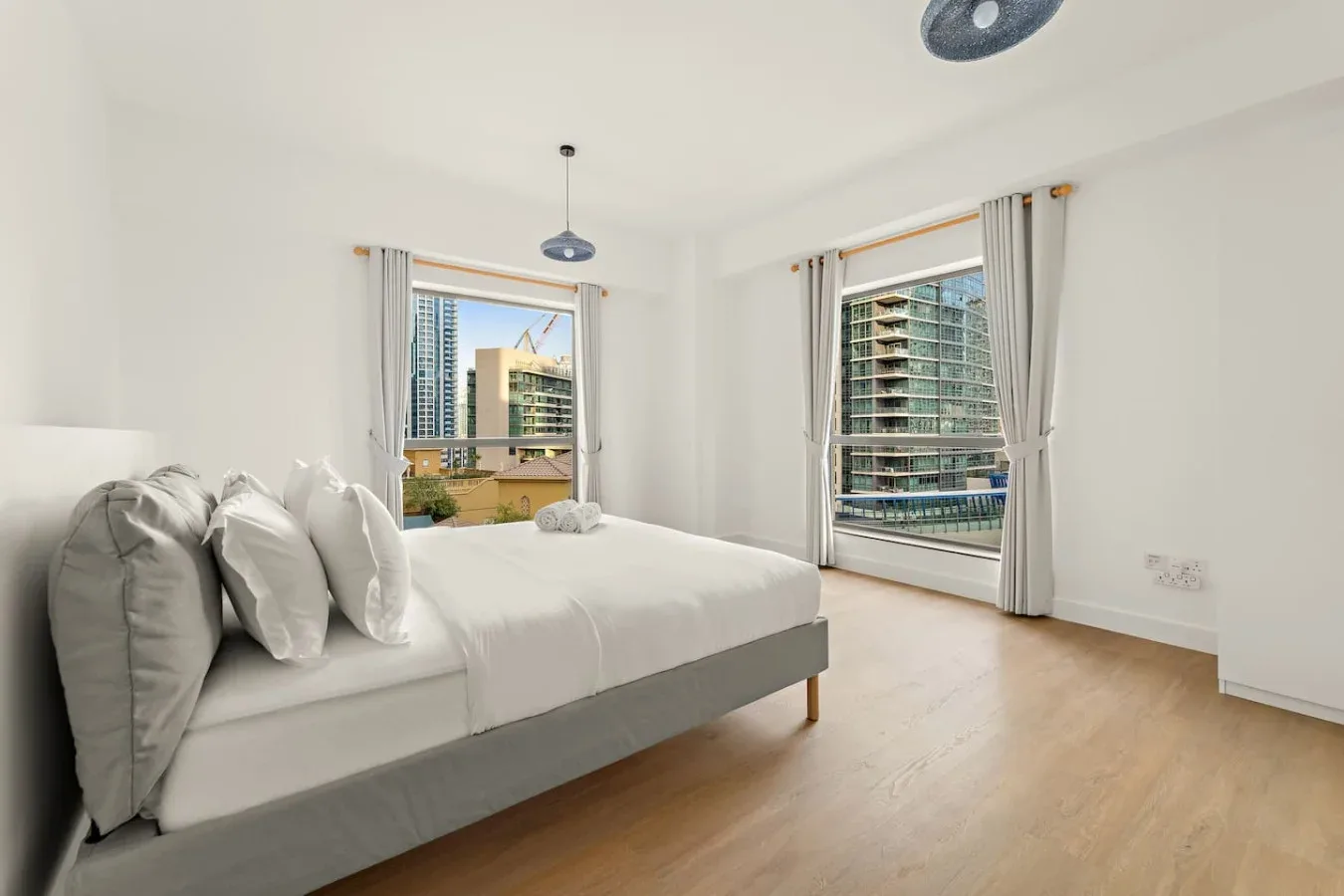Un dormitorio luminoso con una cama junto a dos ventanas grandes.