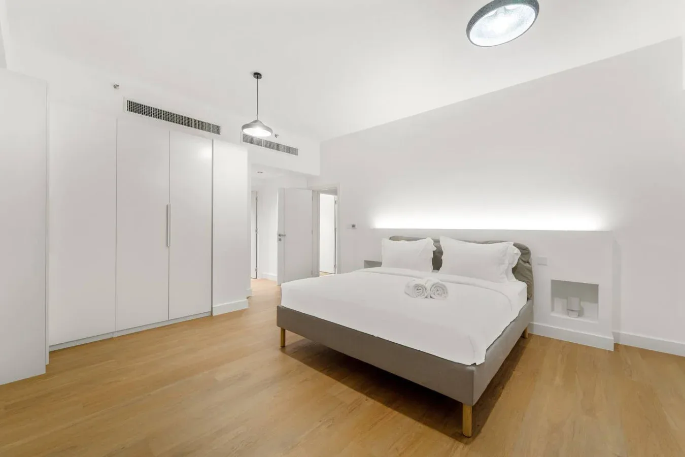 Un dormitorio luminoso con una cama, armarios empotrados y suelo de madera clara.