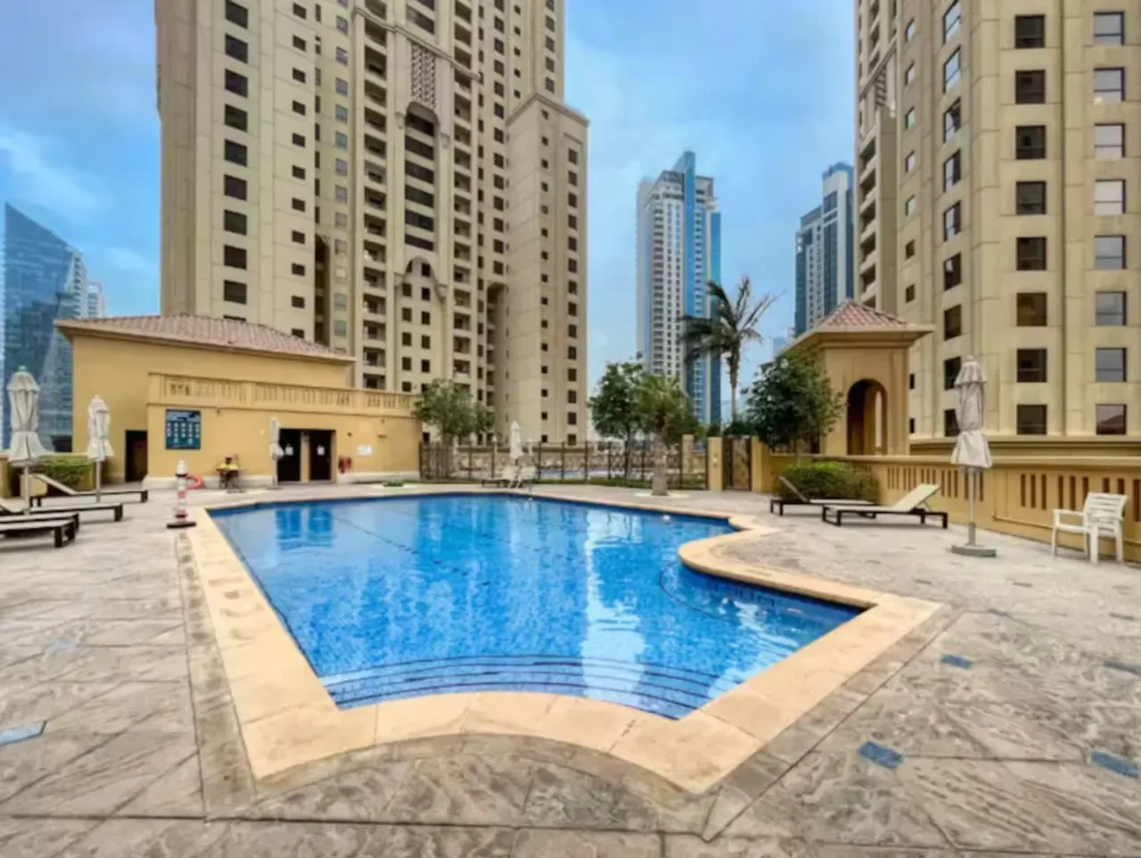 Una piscina al aire libre está rodeada de altas torres residenciales y zonas pavimentadas con asientos.