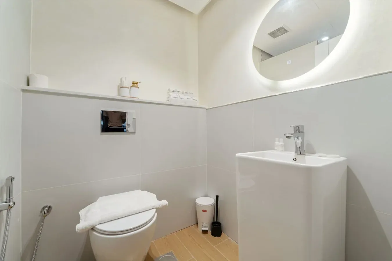 Un baño con inodoro, lavabo y espejo redondo iluminado.