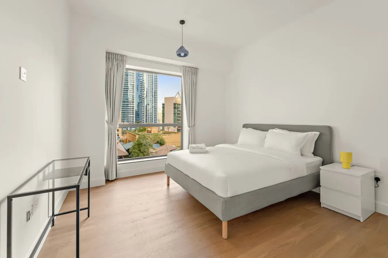 Un dormitorio luminoso con una cama bien hecha junto a una ventana grande.