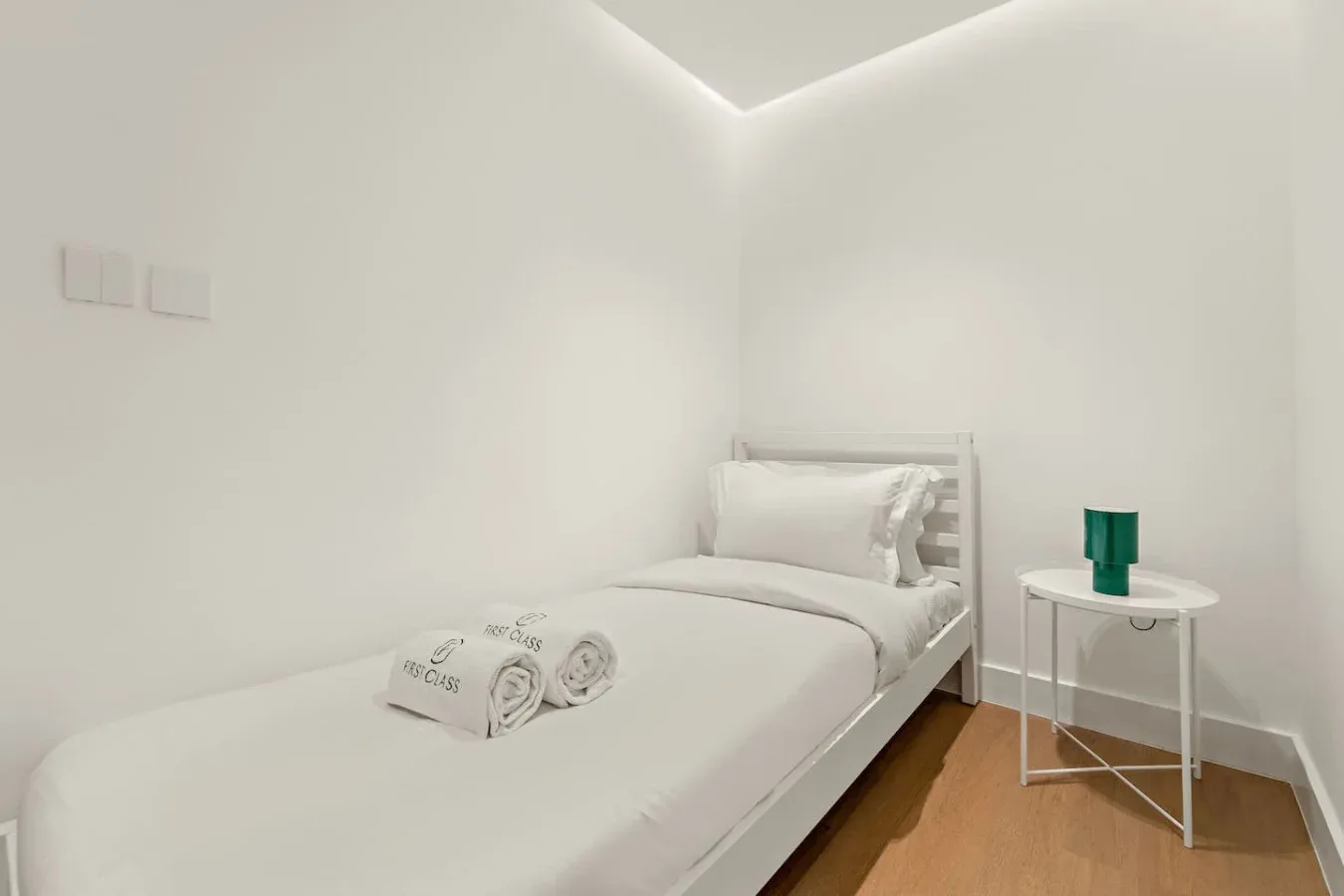 Un dormitorio luminoso con una cama tendida y una pequeña mesa auxiliar.