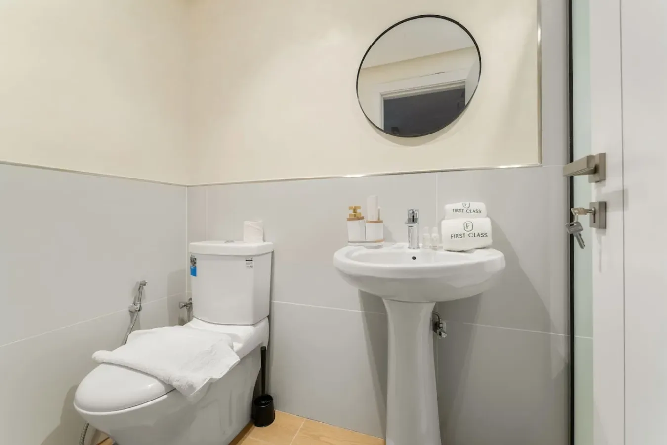 Un baño con lavabo de pedestal, inodoro y espejo redondo en la pared.