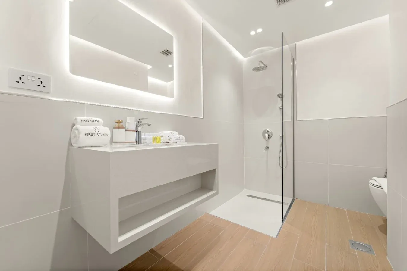 Un baño moderno y luminoso con lavabo, espejo iluminado y ducha de cristal.