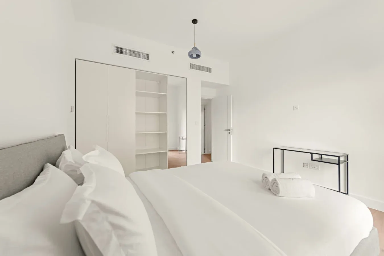 Un dormitorio luminoso con una cama tendida y estantes abiertos.