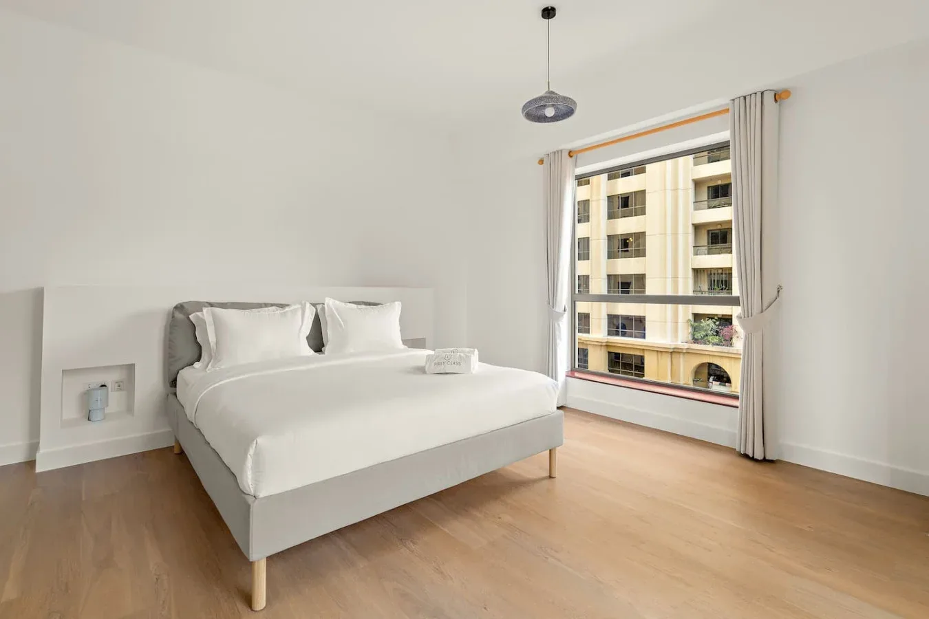 Un dormitorio luminoso con una cama bien tendida junto a una ventana grande.