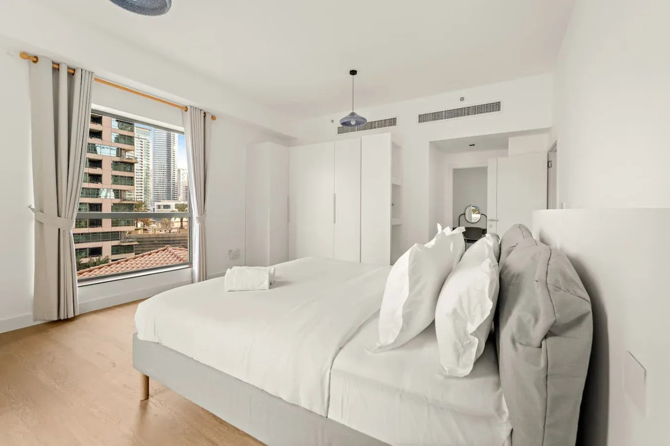 Un dormitorio luminoso con una cama blanca junto a una ventana grande.