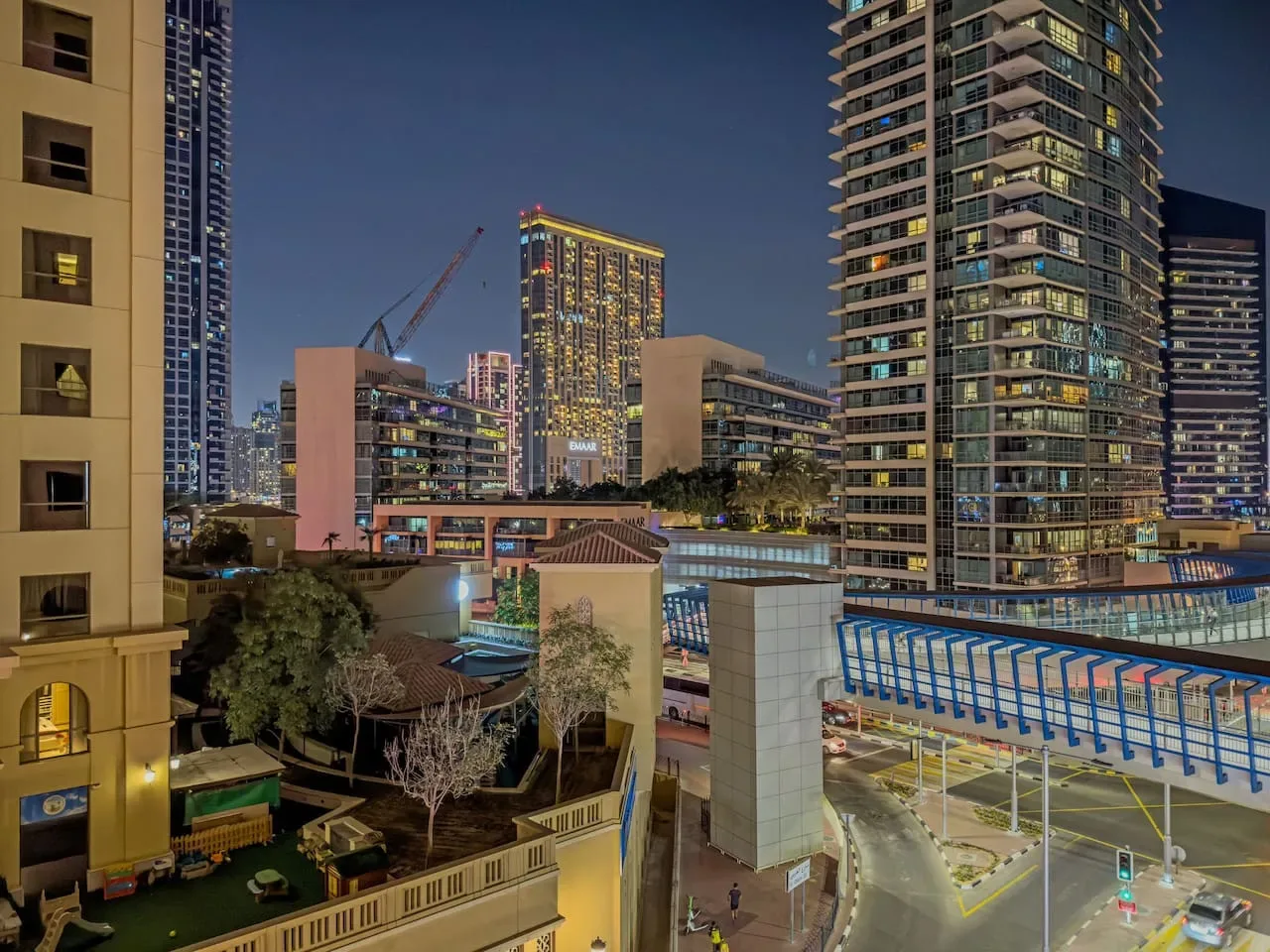 Paisaje urbano nocturno con edificios altos iluminados y una grúa de construcción.