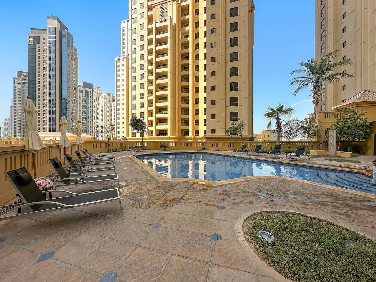 Una piscina al aire libre está rodeada por una terraza pavimentada y edificios altos.