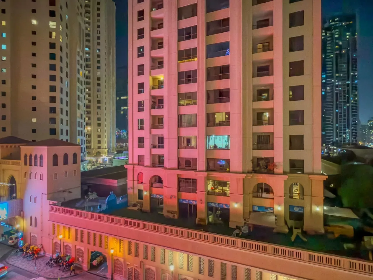 Una escena nocturna de la ciudad muestra edificios altos iluminados sobre una calle.