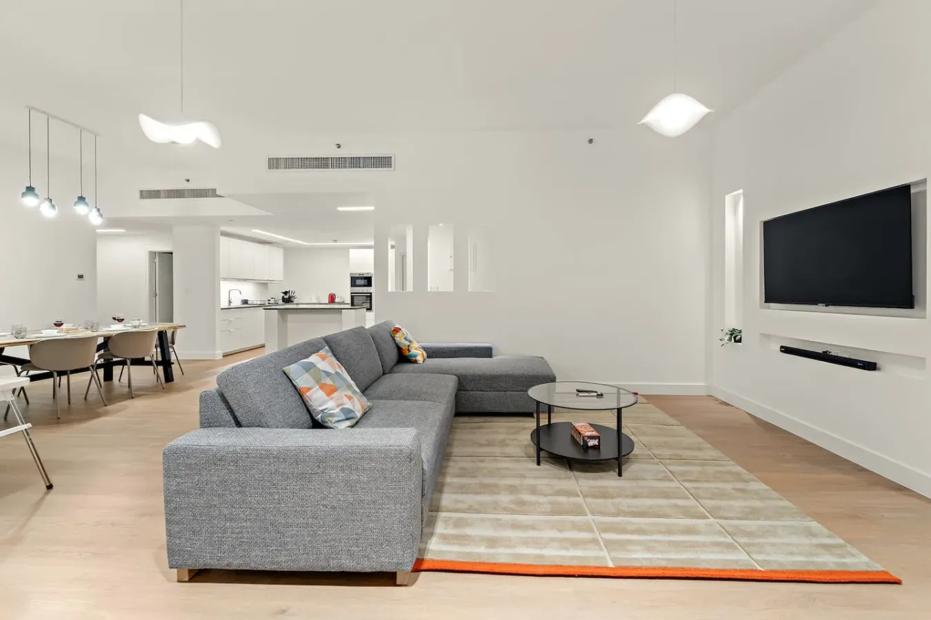 Una sala luminosa con asientos grises, una mesa de centro y un televisor en la pared.