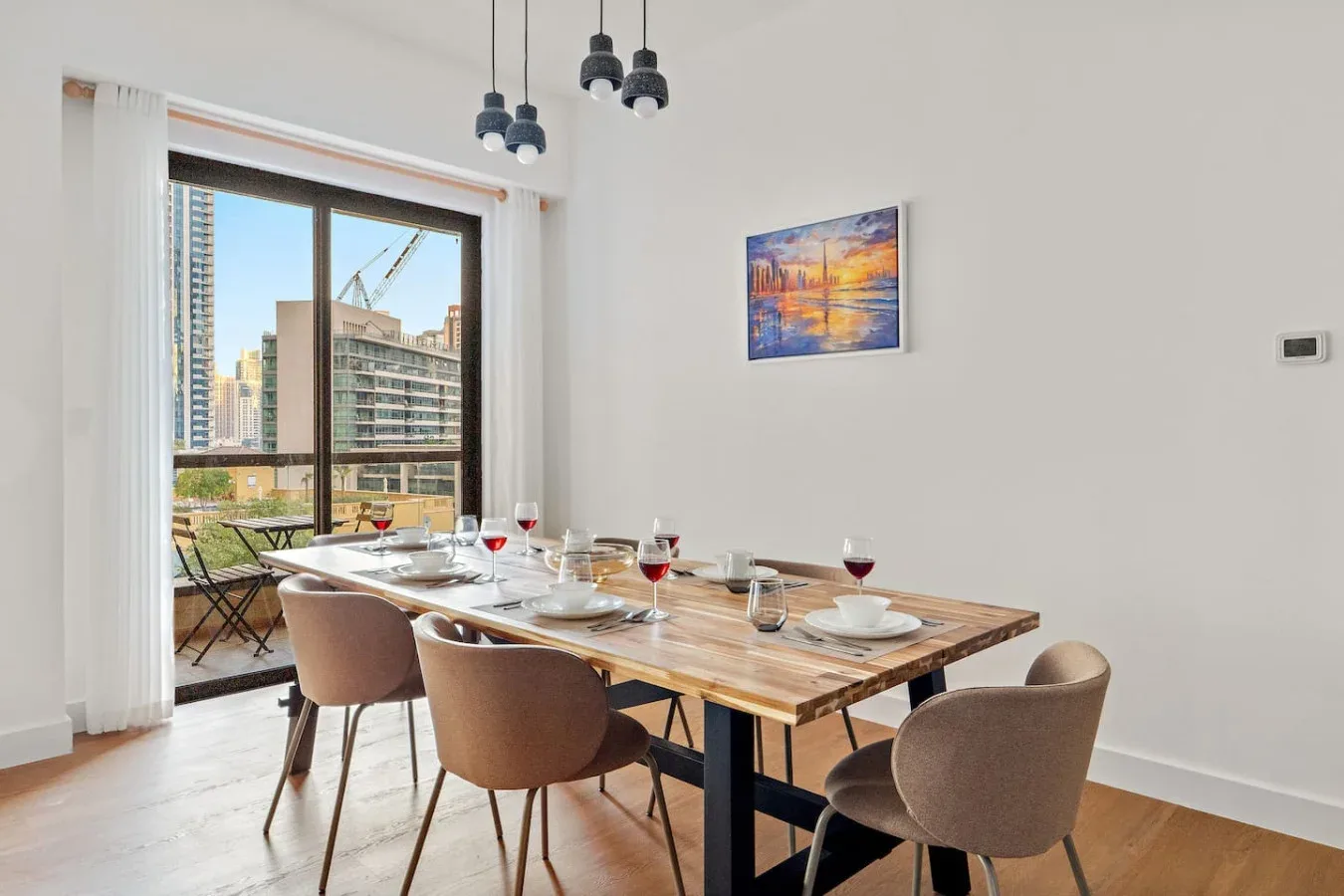 Comedor con una mesa de madera puesta con vajilla junto a grandes ventanales.