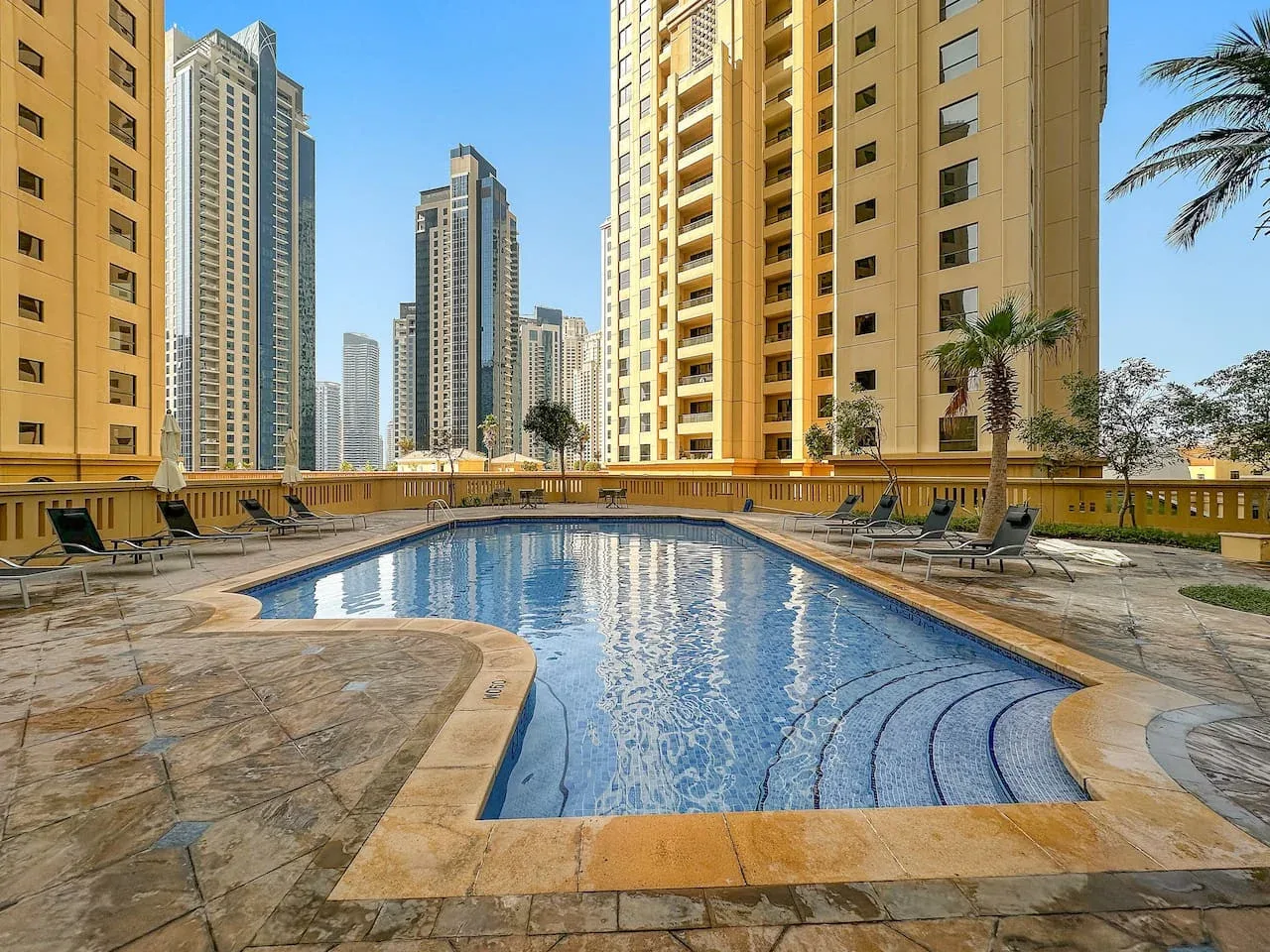 Una piscina al aire libre está rodeada de edificios altos y palmeras.