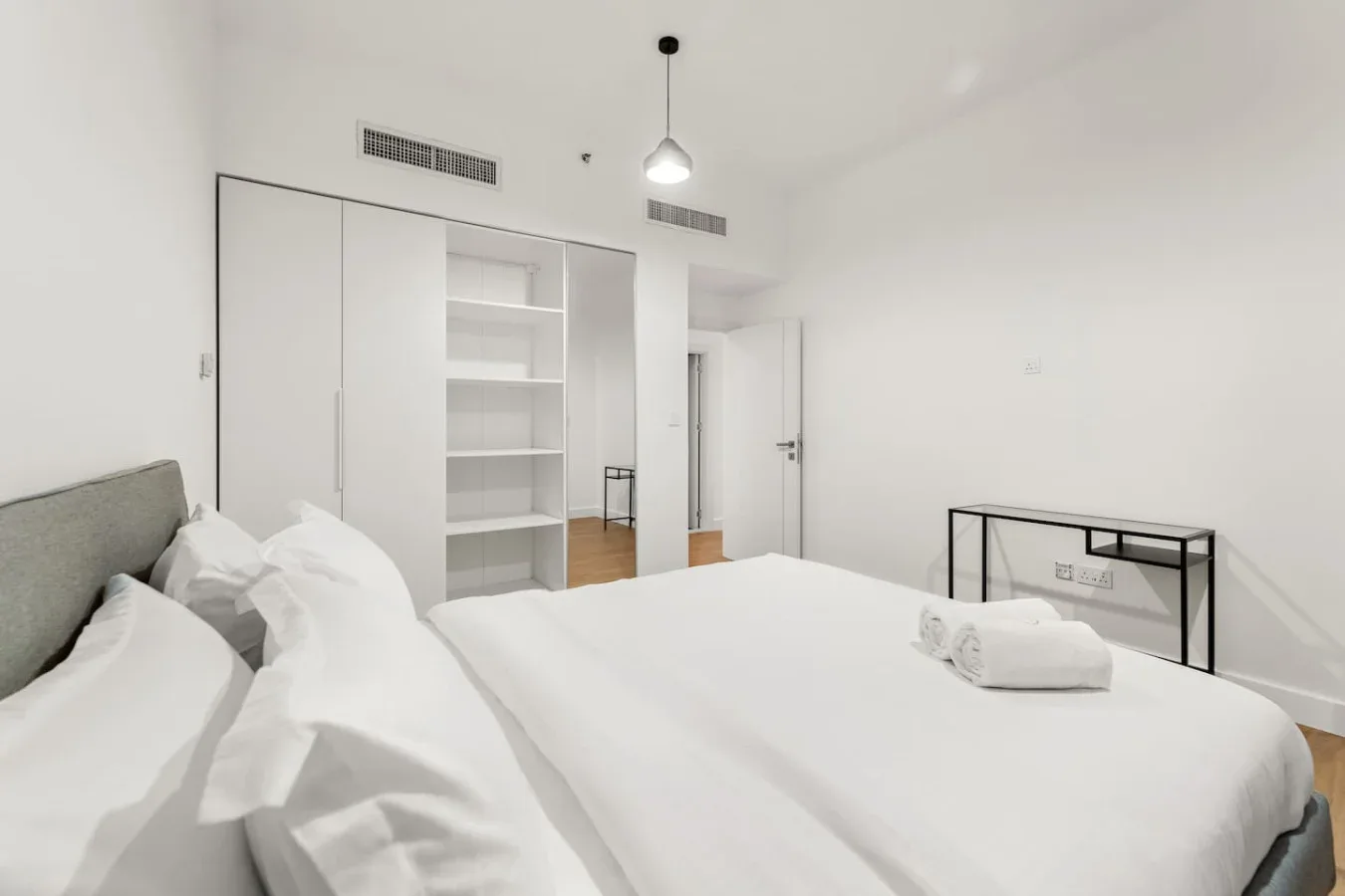 Un dormitorio luminoso con ropa de cama blanca y estanterías empotradas.