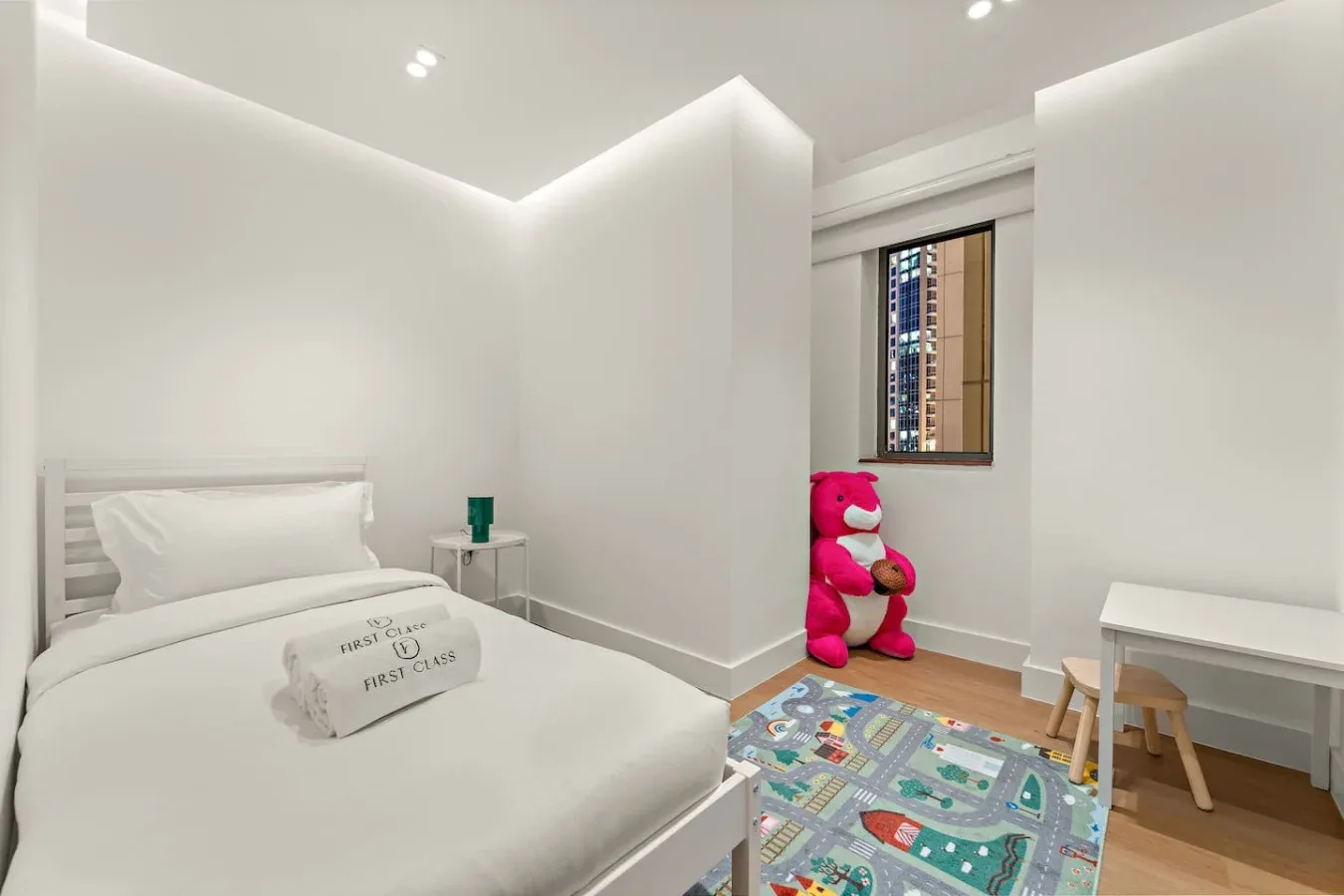 Un dormitorio luminoso con una cama blanca y una alfombra de juegos colorida.