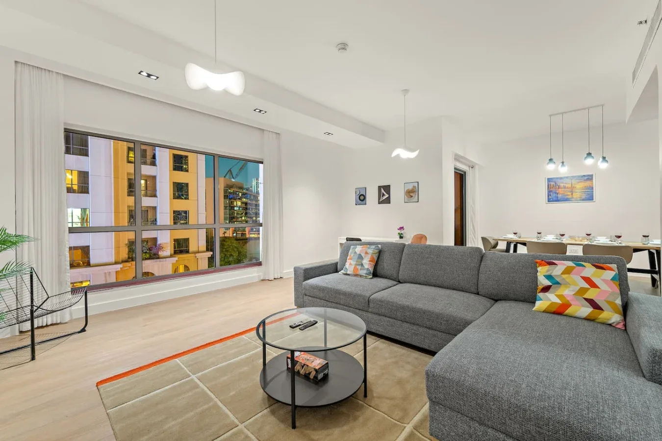 Una sala luminosa con asientos grises, una mesa de centro de vidrio y una ventana grande.