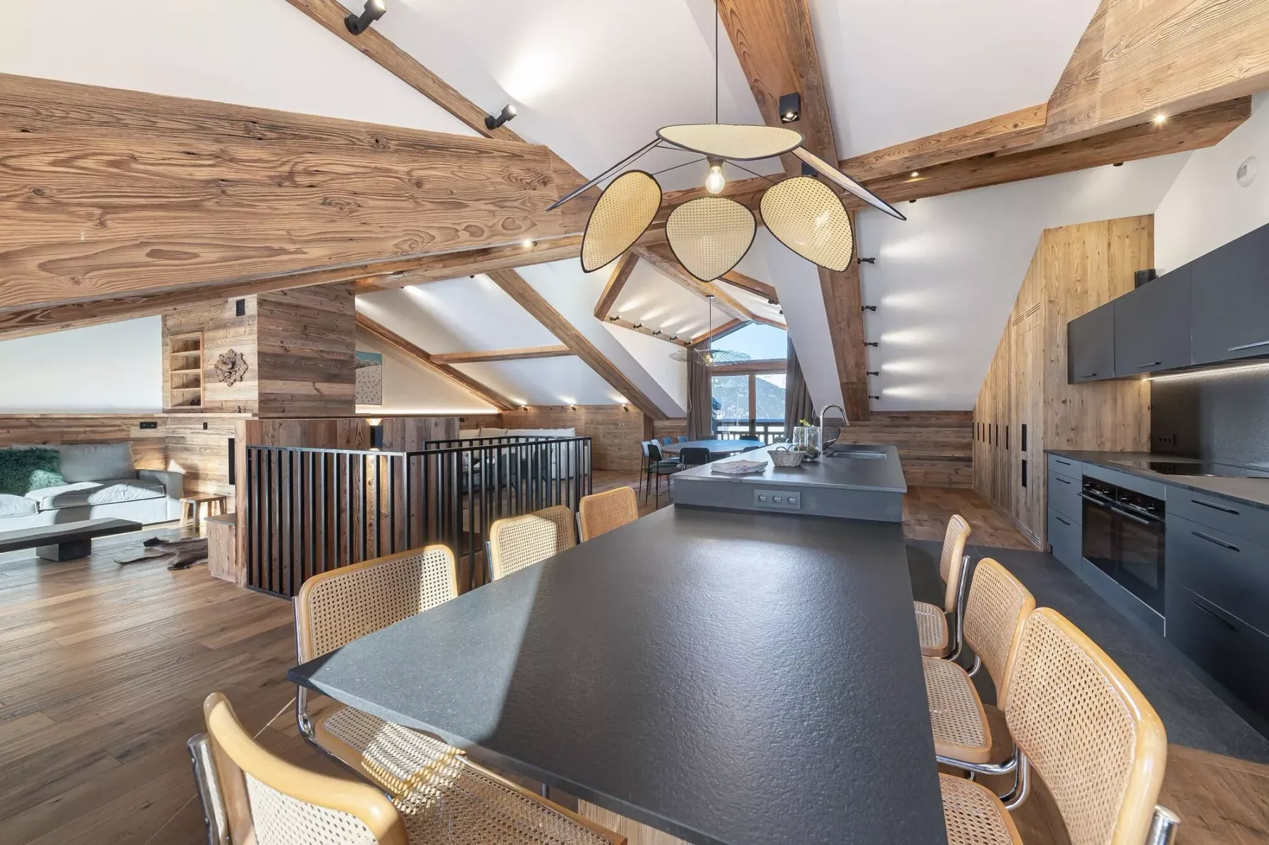 A dining area with a long table and seating beneath exposed timber beams.