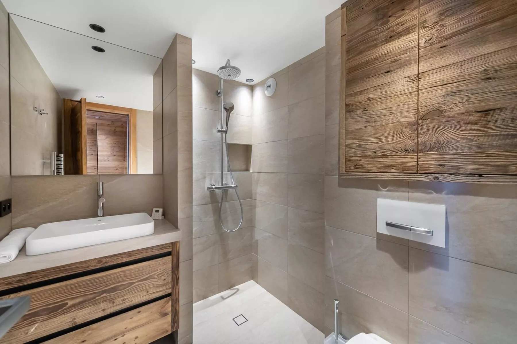 Un baño revestido de azulejos con lavabo, inodoro suspendido y ducha.