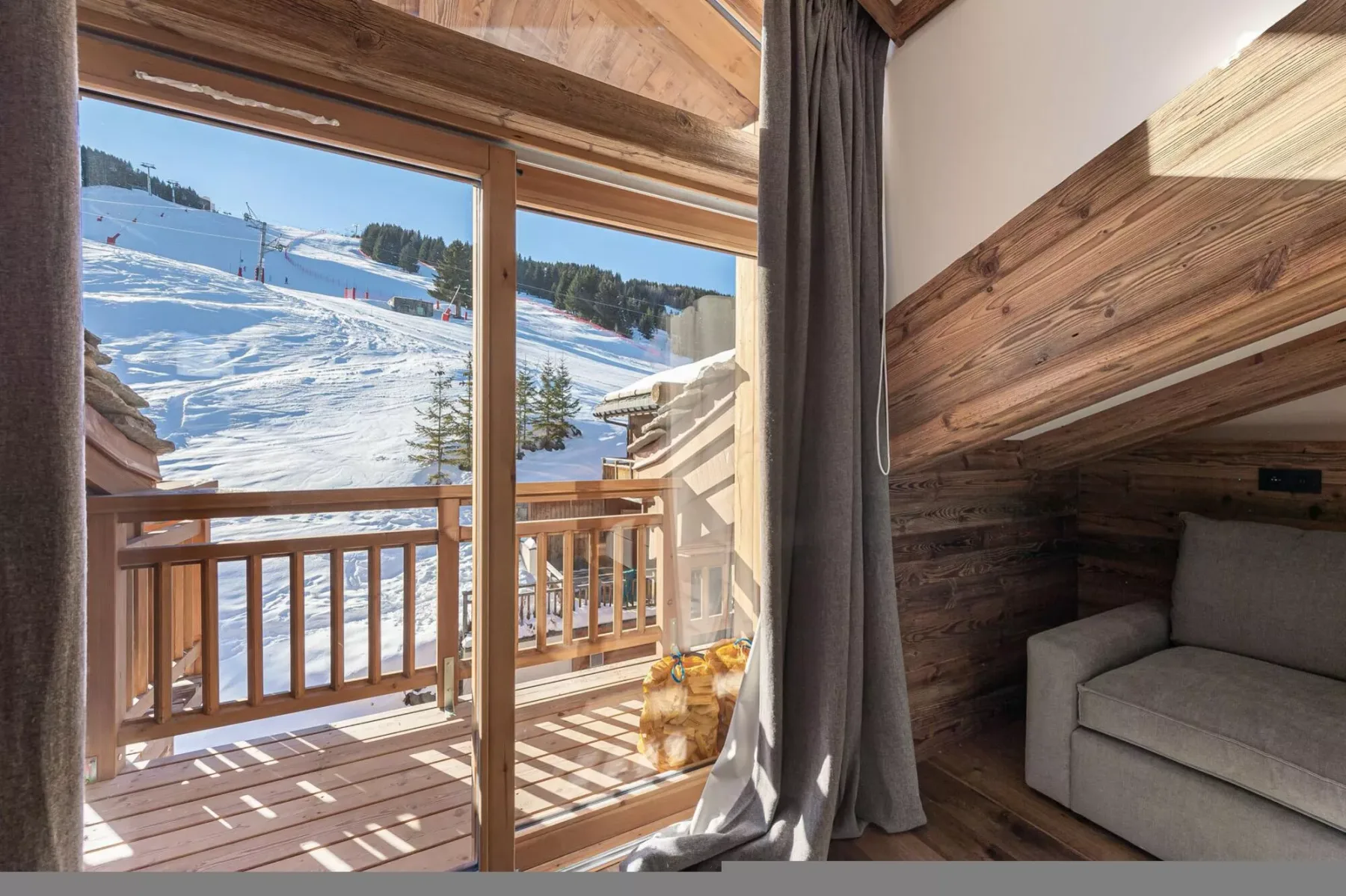 Una zona de estar revestida de madera da a un balcón con vistas a una pista nevada.