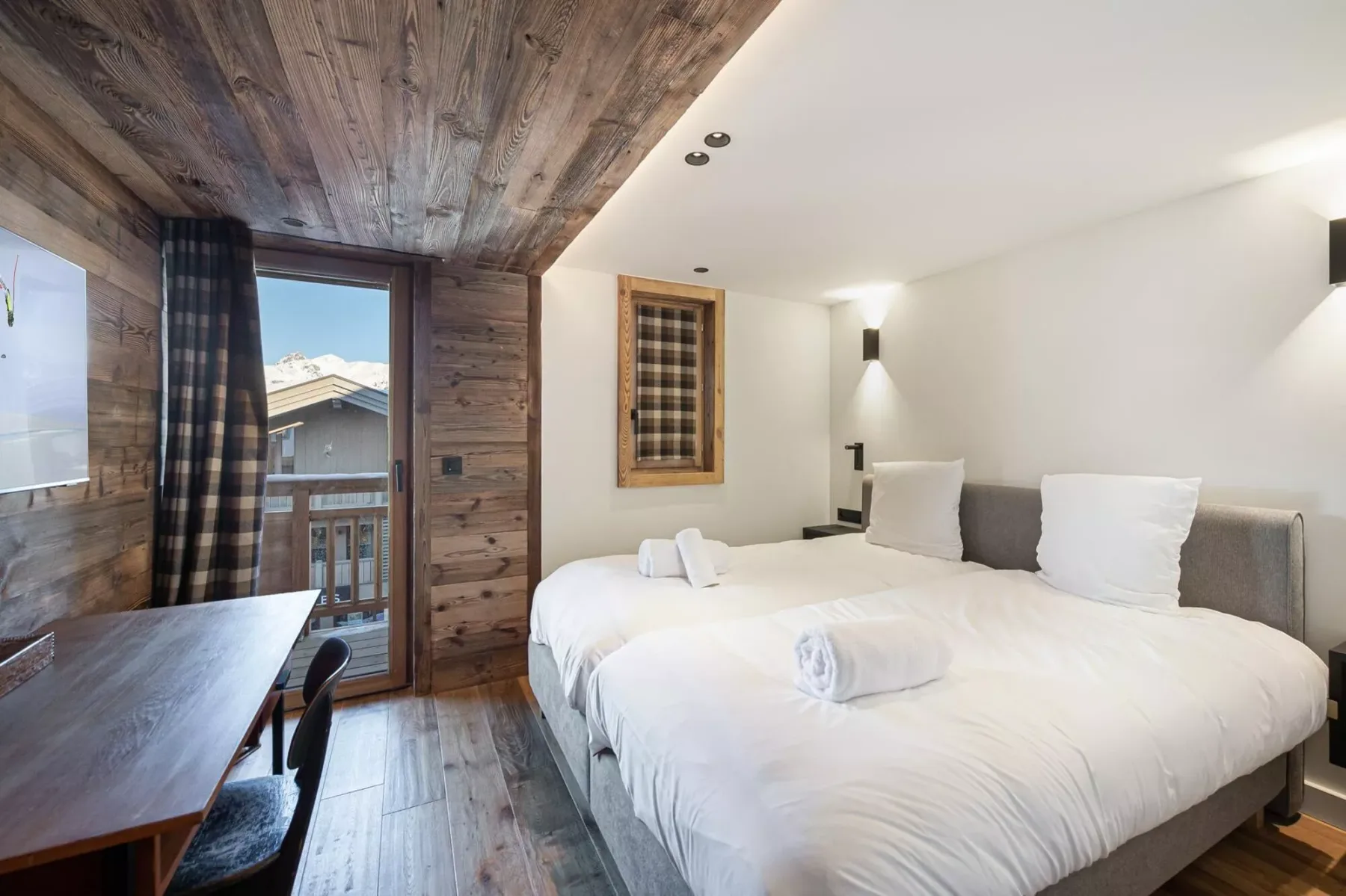 Dormitorio con una cama grande junto a un escritorio de madera y una puerta de balcón.