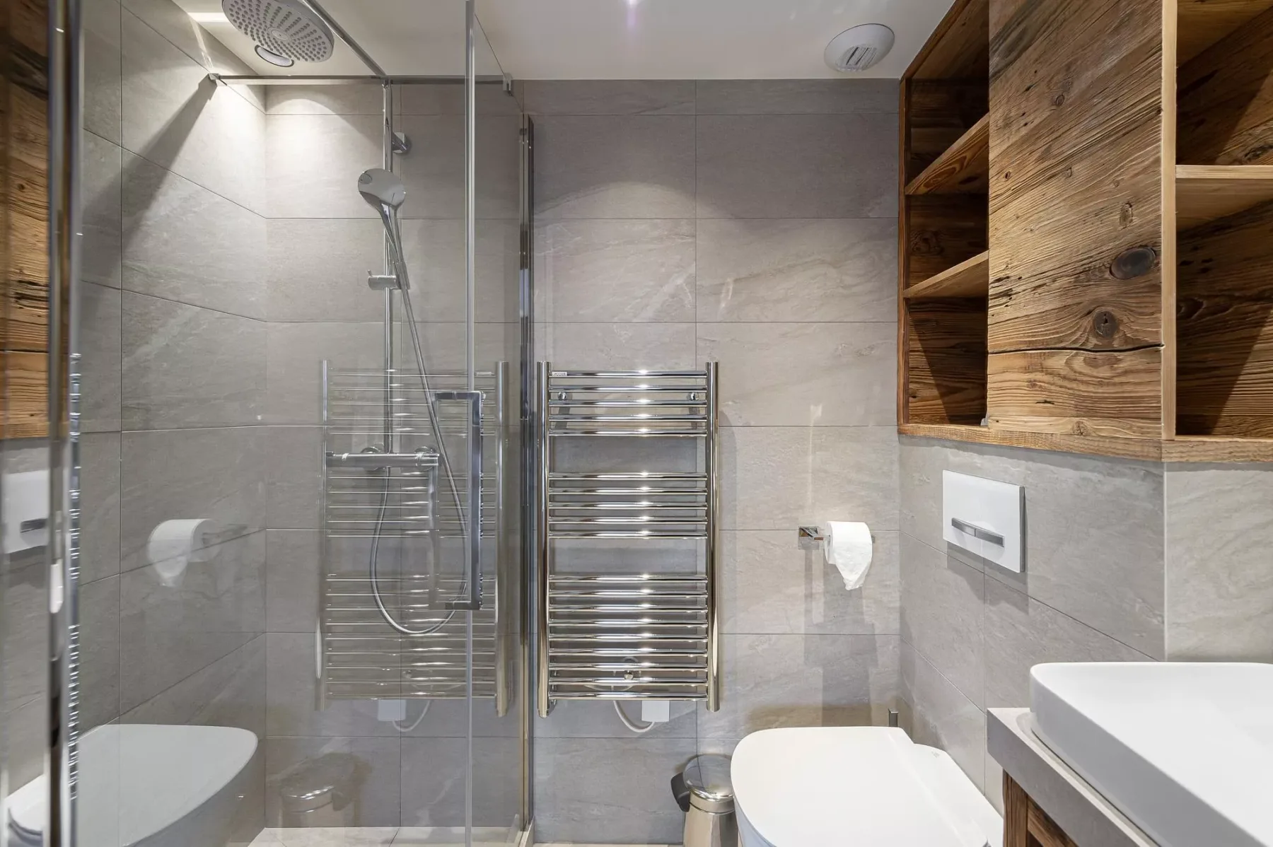 Un baño con azulejos, una ducha de vidrio y un toallero calefactado en la pared.