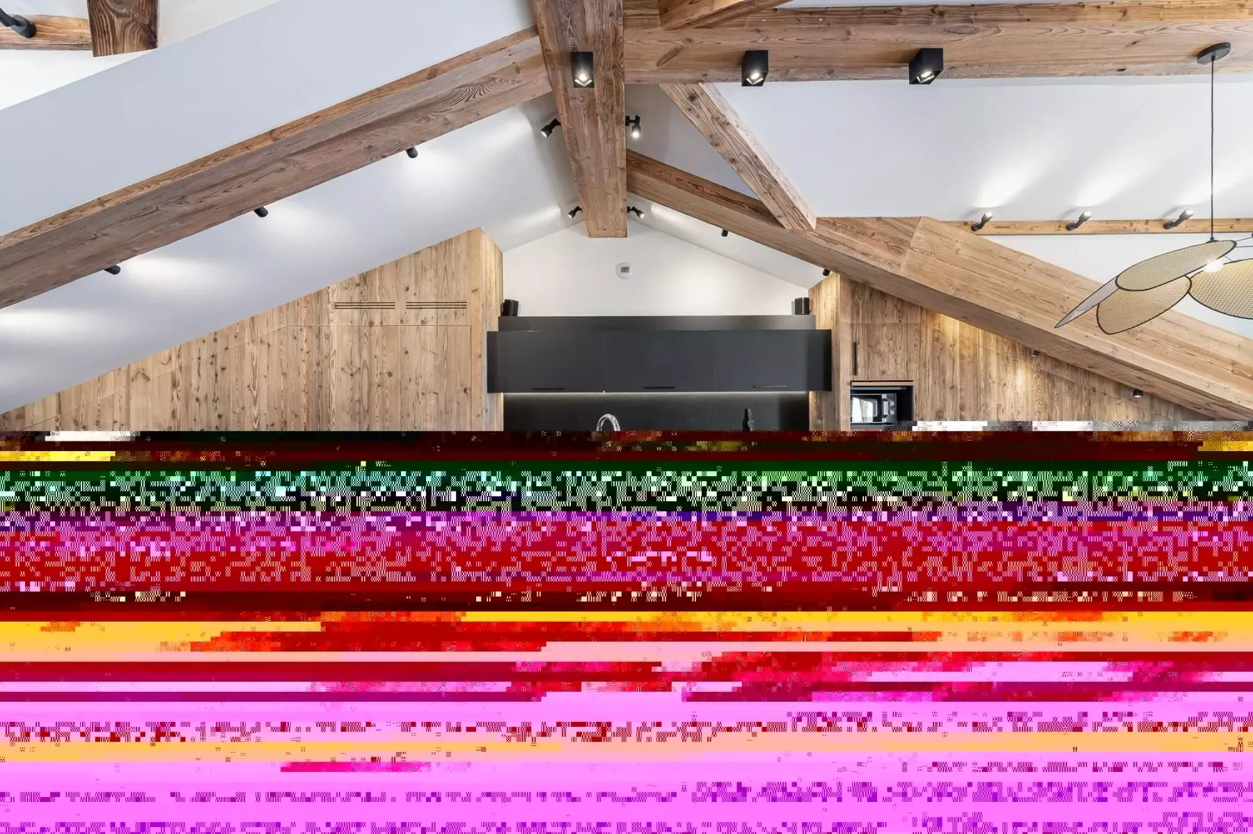 A kitchen beneath a timber ceiling, with wooden cabinets and a dark range hood.