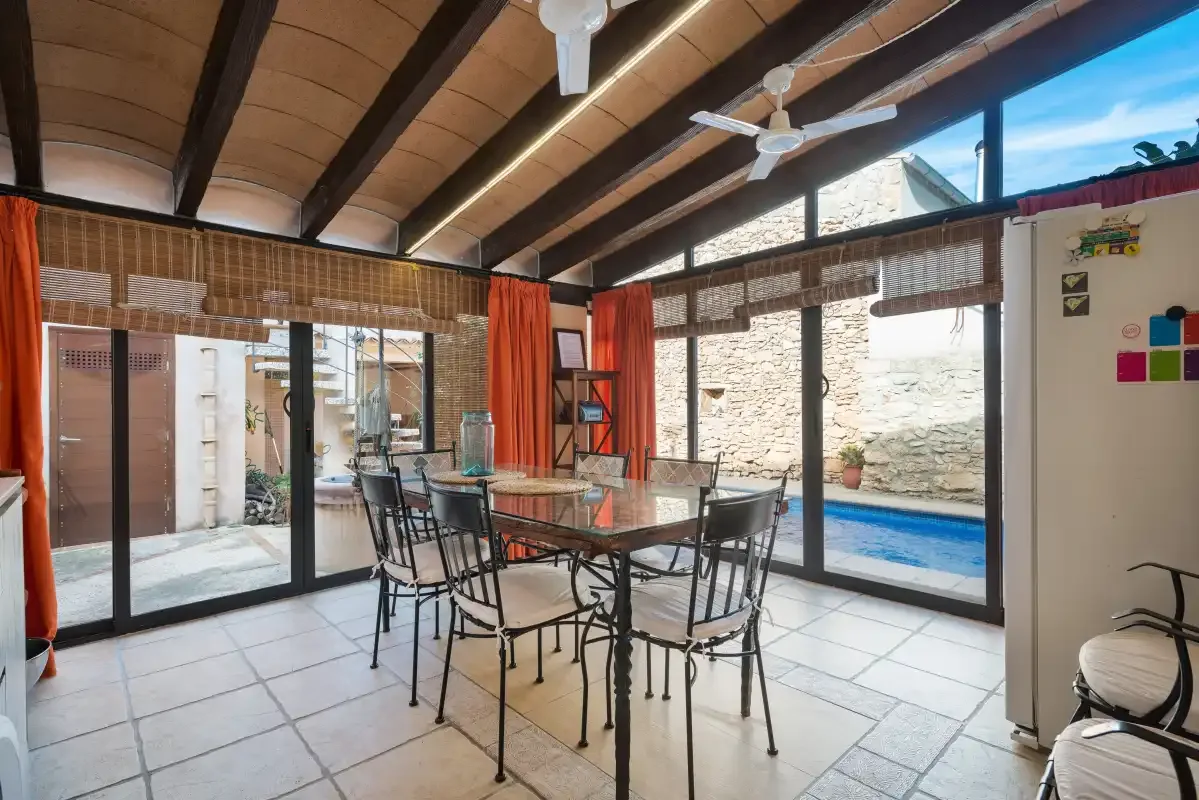 A dining area with a table and chairs opens onto a patio and swimming pool.