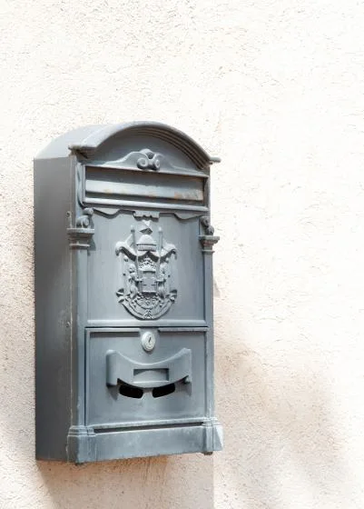 An ornate metal mailbox is mounted on a light-colored exterior wall.