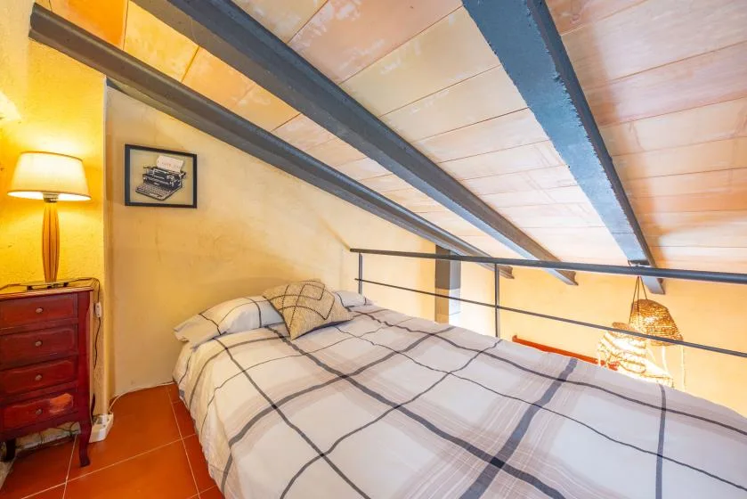 A bedroom with a bed beneath a sloped ceiling and exposed beams.