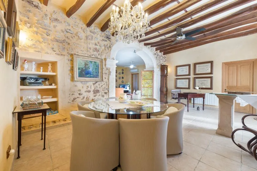 A dining room with a round table and chairs beneath exposed wooden ceiling beams.