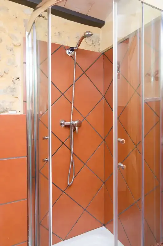 A shower with orange tiled walls and a handheld showerhead.
