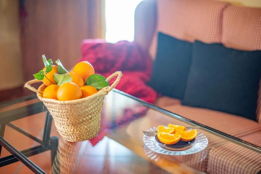 A living room seating area with a glass coffee table and a basket of oranges.