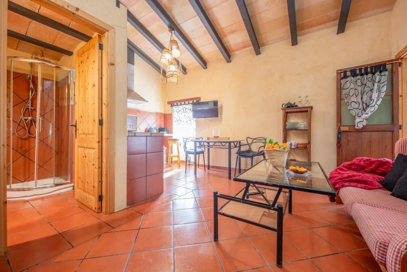 A rustic living and dining area with a glass coffee table and exposed ceiling beams.