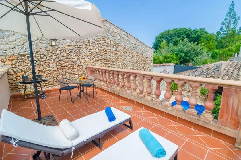 A sunny terrace with lounge seating, a large umbrella, and a stone wall.