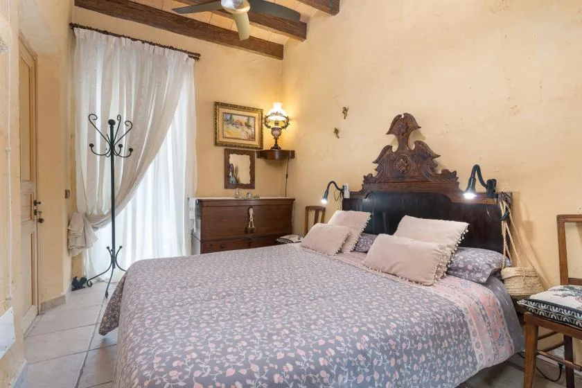 A bedroom with a large bed, sheer curtains, and exposed ceiling beams.