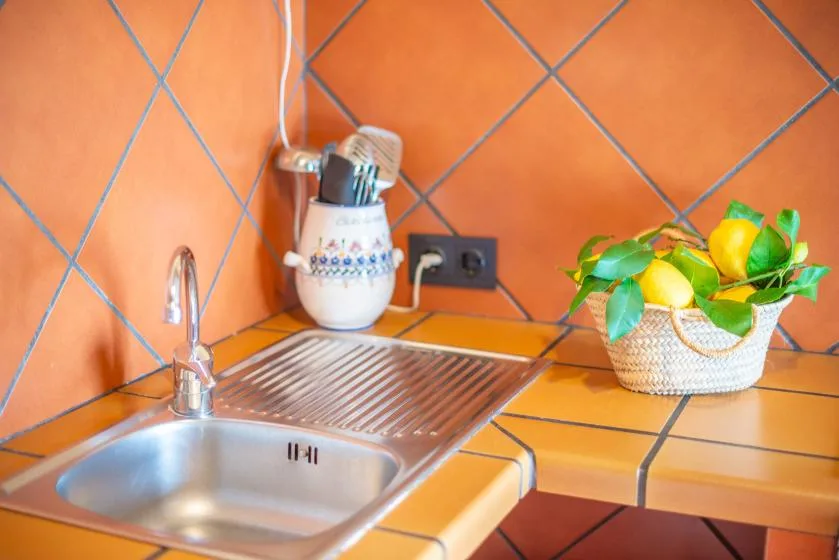 A tiled kitchen counter with a stainless steel sink, draining board, and basket of lemons.