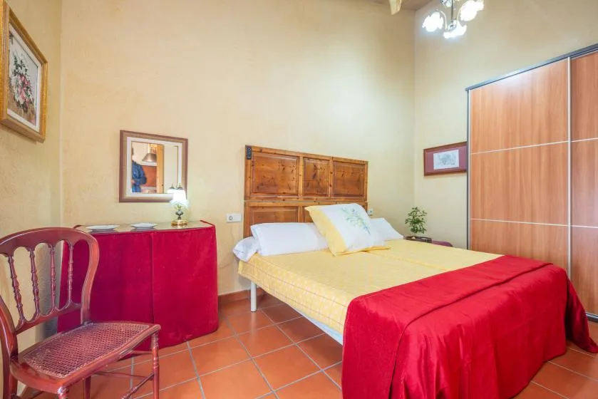 A bedroom with a bed, a red-covered desk, and a large wardrobe.