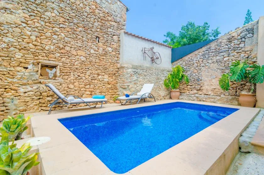 A blue swimming pool sits in a stone-walled courtyard with lounge seating.