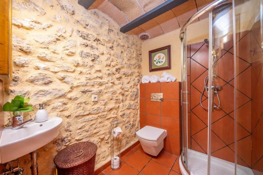 A bathroom with a stone wall, wall-mounted sink, toilet, and glass shower.