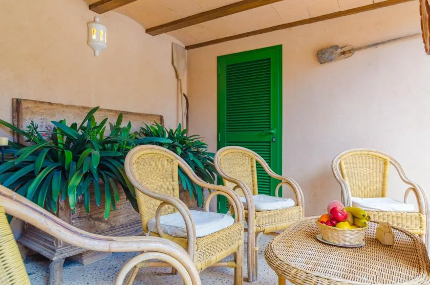A covered patio with wicker seating, potted plants, and a green door.