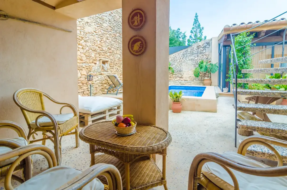 A covered patio with wicker seating overlooks a small pool and stone courtyard.