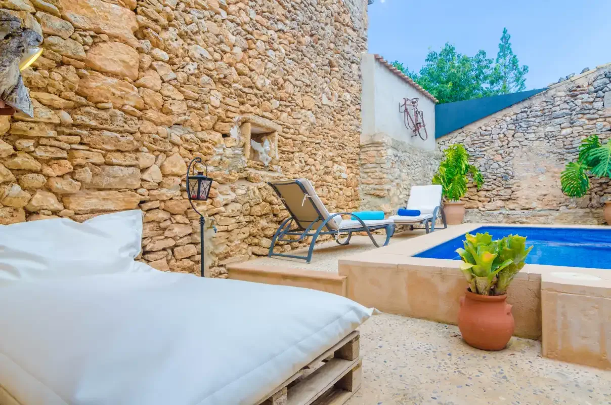 A stone-walled outdoor pool area with lounge seating and potted plants.