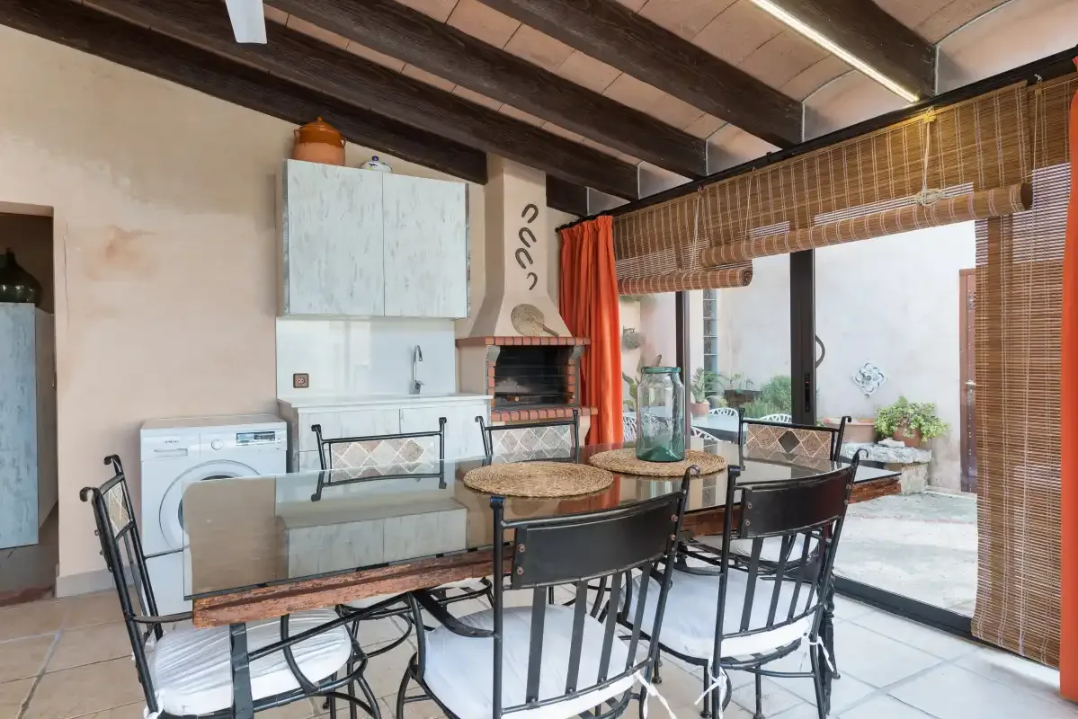 A dining area with a table and chairs sits beside a kitchen and sliding glass doors.