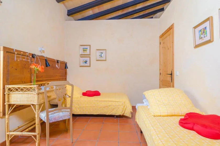 A bedroom with yellow-covered beds, wooden furniture, and exposed ceiling beams.