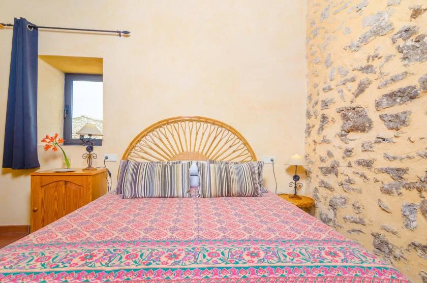A bedroom with a patterned bedspread and a woven headboard beside a stone wall.