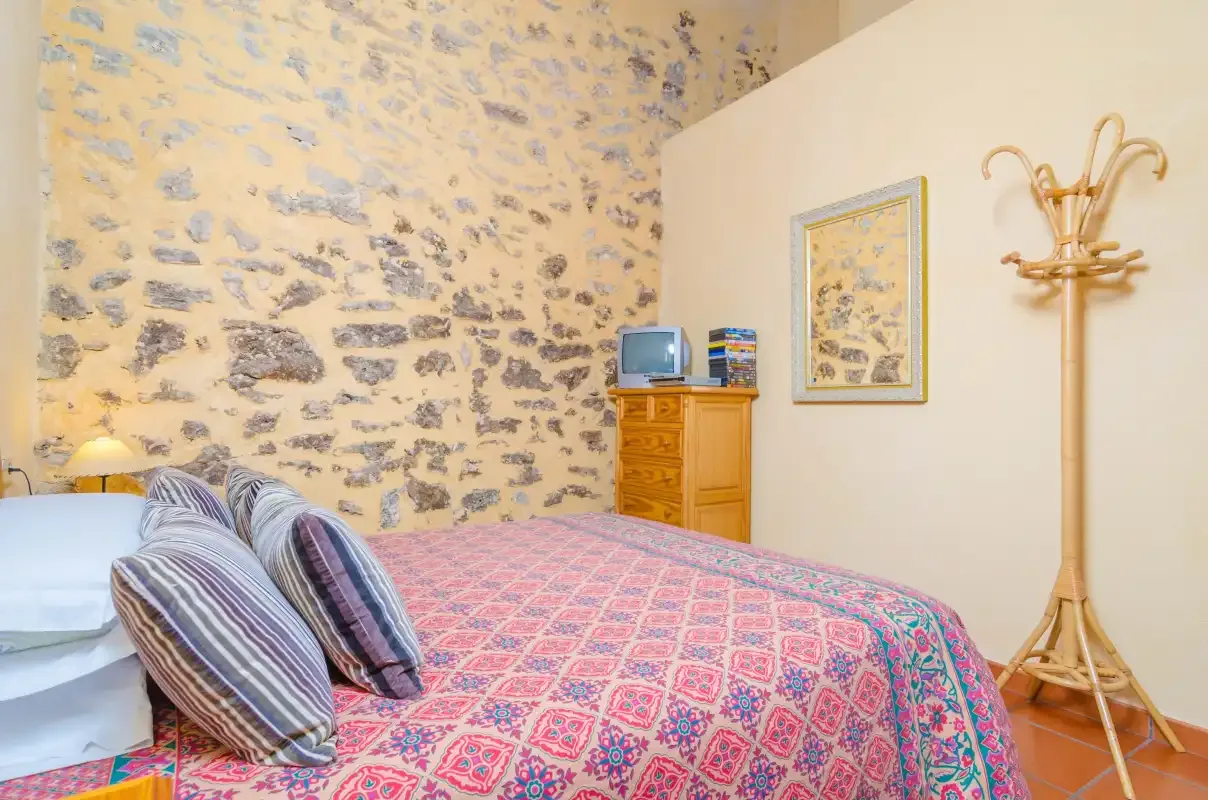 A bedroom with a patterned bedspread and exposed stone wall.