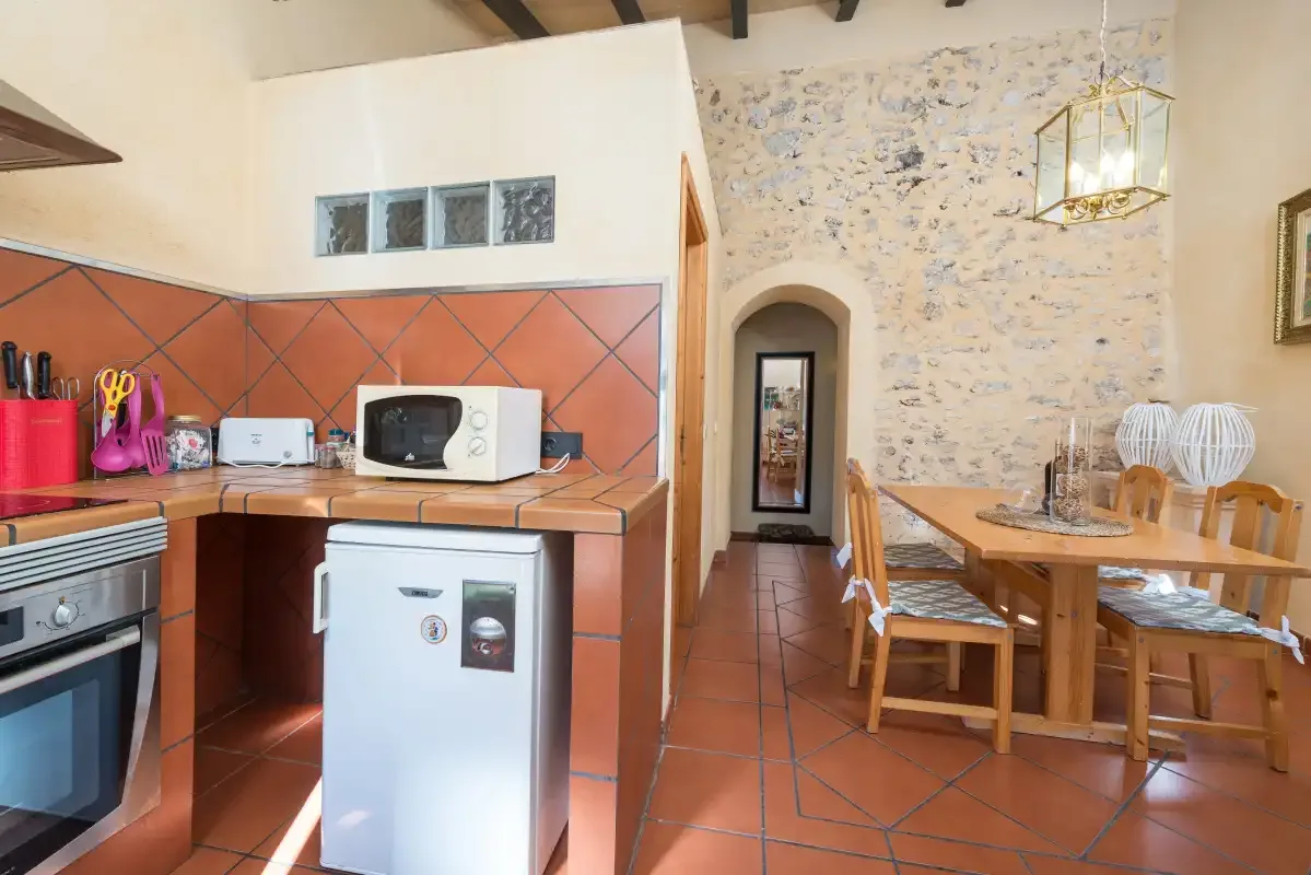 A kitchen and dining area with terracotta-colored tile floors and exposed ceiling beams.