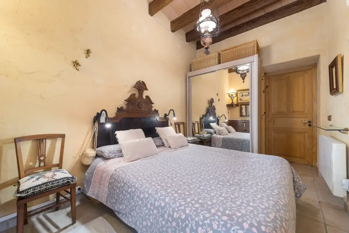 A bedroom with a large bed, mirrored wardrobe, and wooden ceiling beams.