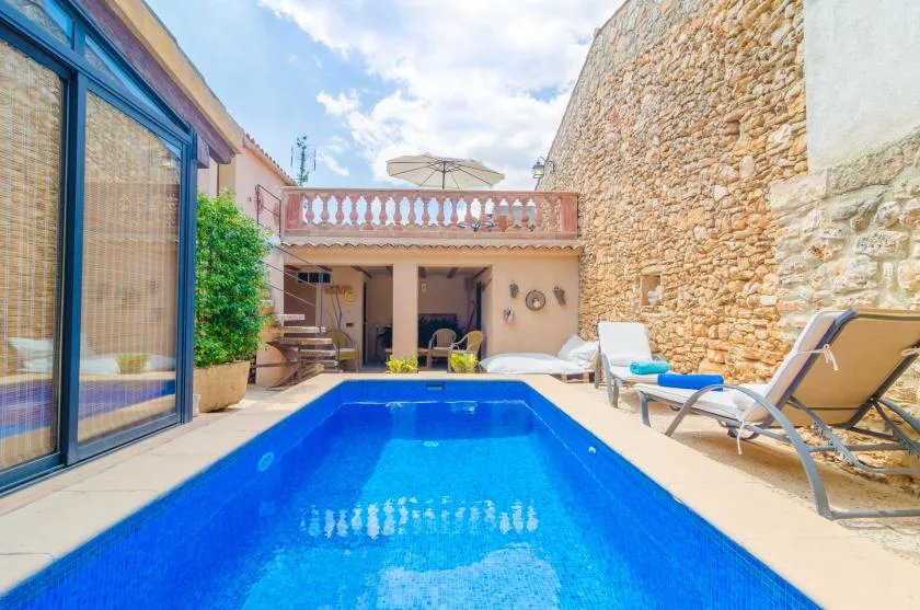 A small outdoor swimming pool sits beside a stone wall and patio seating.
