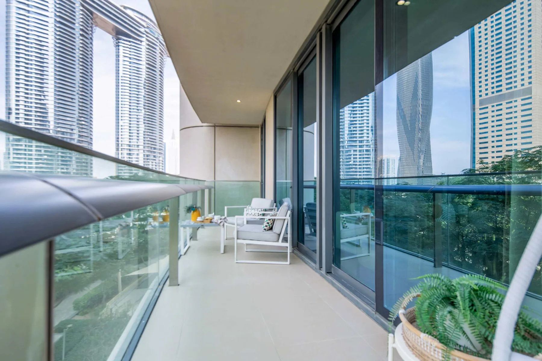 A balcony with glass railings and seating overlooks nearby high-rise buildings.